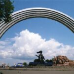 Giant proletarians celebrate under a stainless steel rainbow next to a funfair, Kiev.